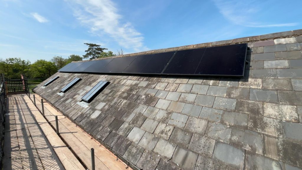 Finished solar panel installation on The Hayloft's slate roof, showing sleek black panels aligned with skylights under clear blue sky.