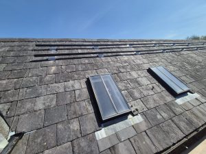 Slate roof at The Hayloft showing solar panel mounting rails and skylights during installation process.